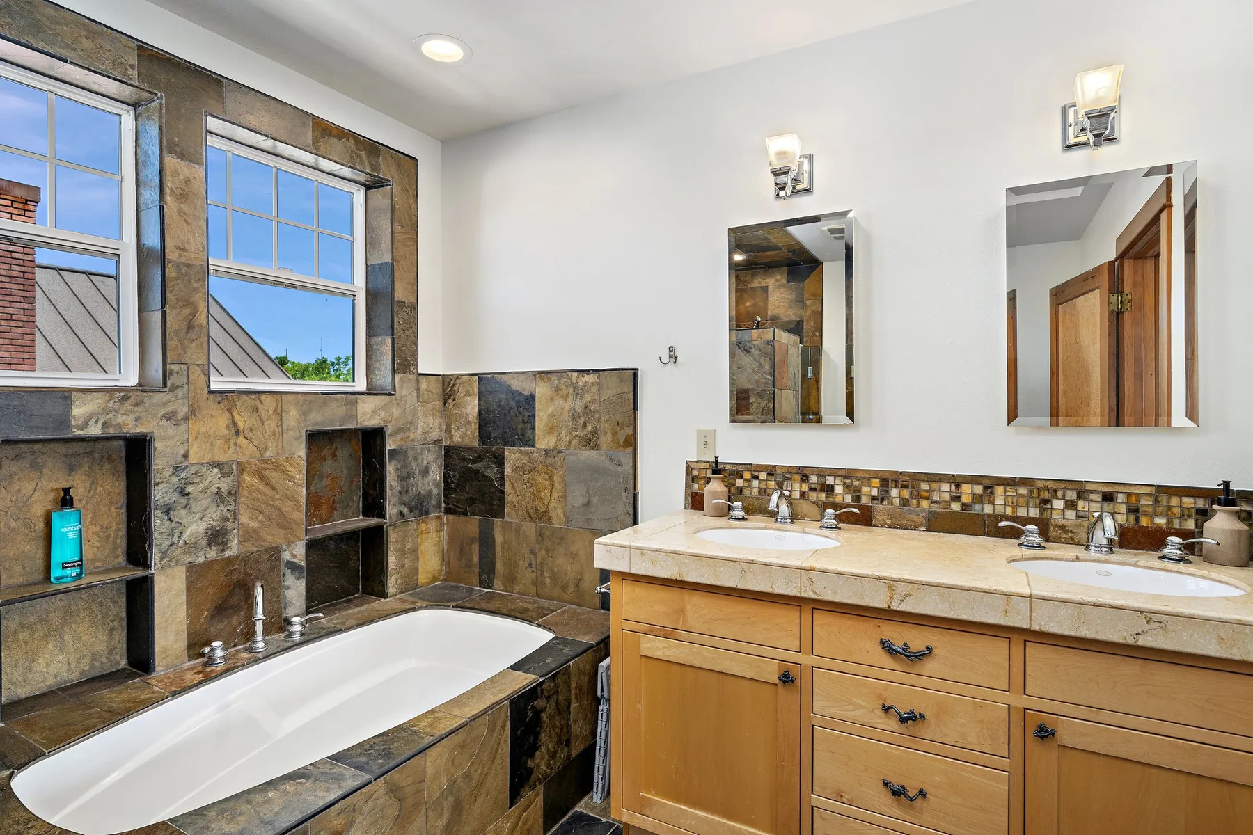 Un baño con bañera, ventanas y un mueble con dos lavabos.
