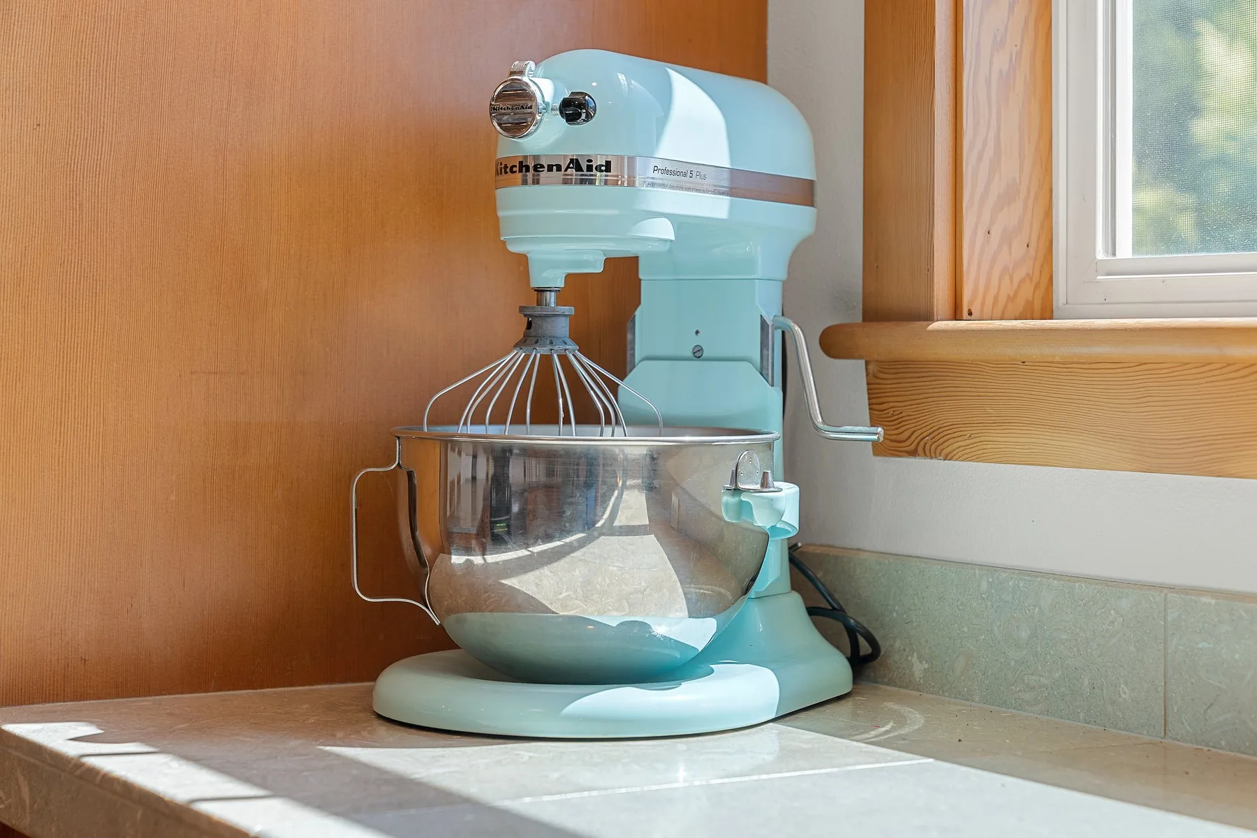 Una batidora de pedestal está sobre la encimera de una cocina, debajo de una ventana.