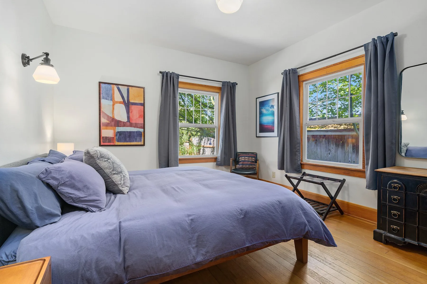 Dormitorio con una cama grande, dos ventanas y cuadros en la pared.