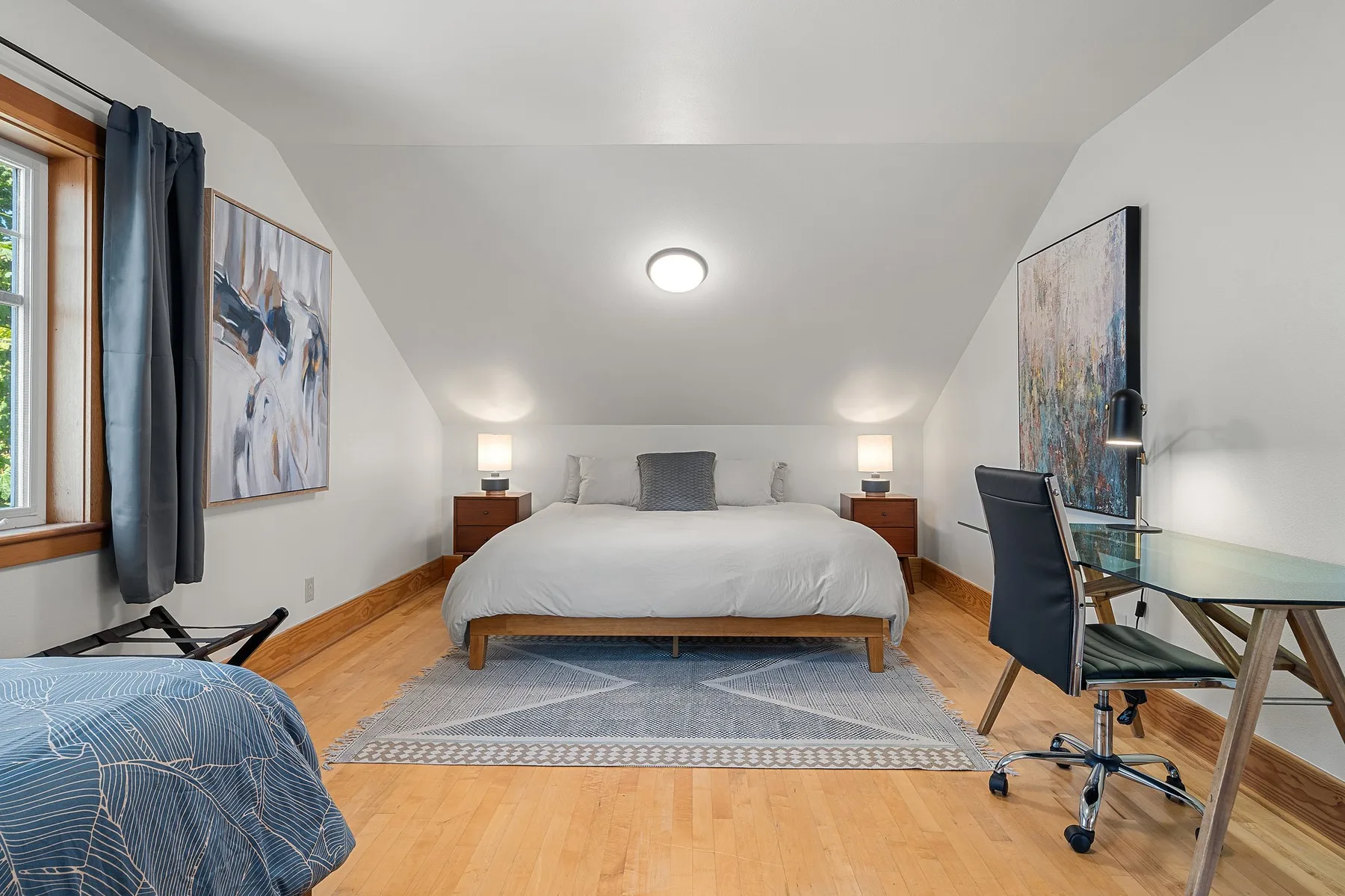 Un dormitorio luminoso con una cama arreglada, mesitas de noche y un escritorio.
