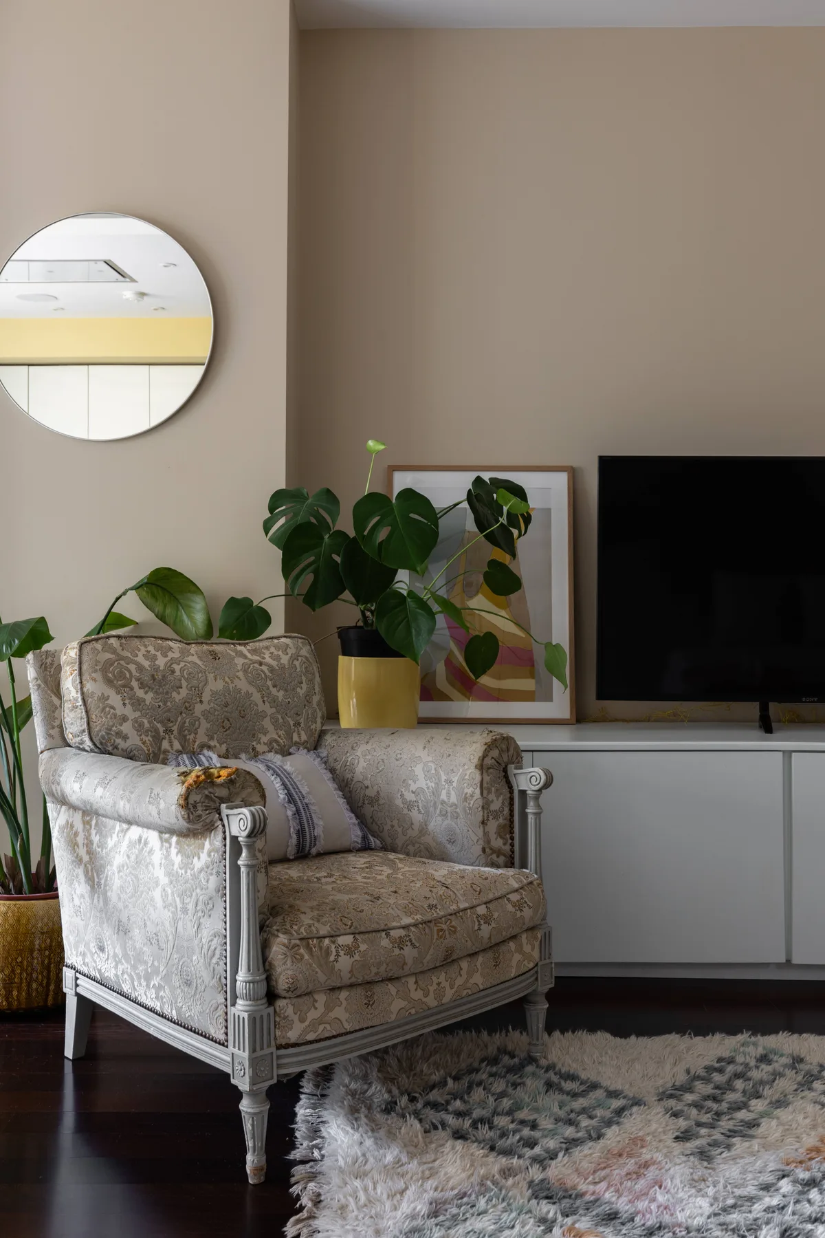 Una zona de estar con un sillón estampado, plantas y un televisor.