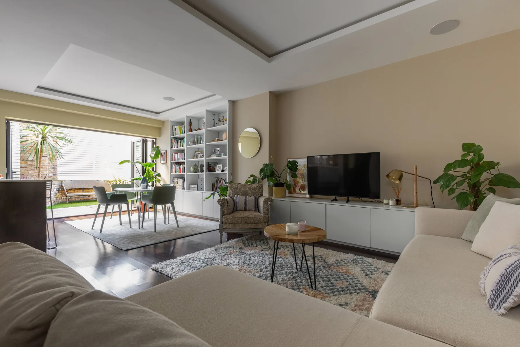 Una sala luminosa con comedor, grandes ventanas y asientos alrededor de un televisor.