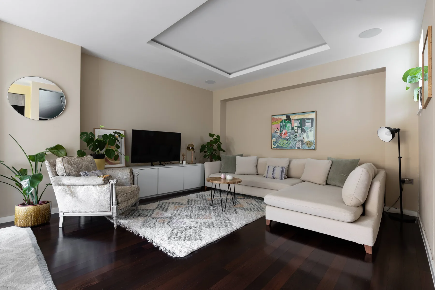 Una sala de estar luminosa con asientos en forma de L, una alfombra y varias plantas.