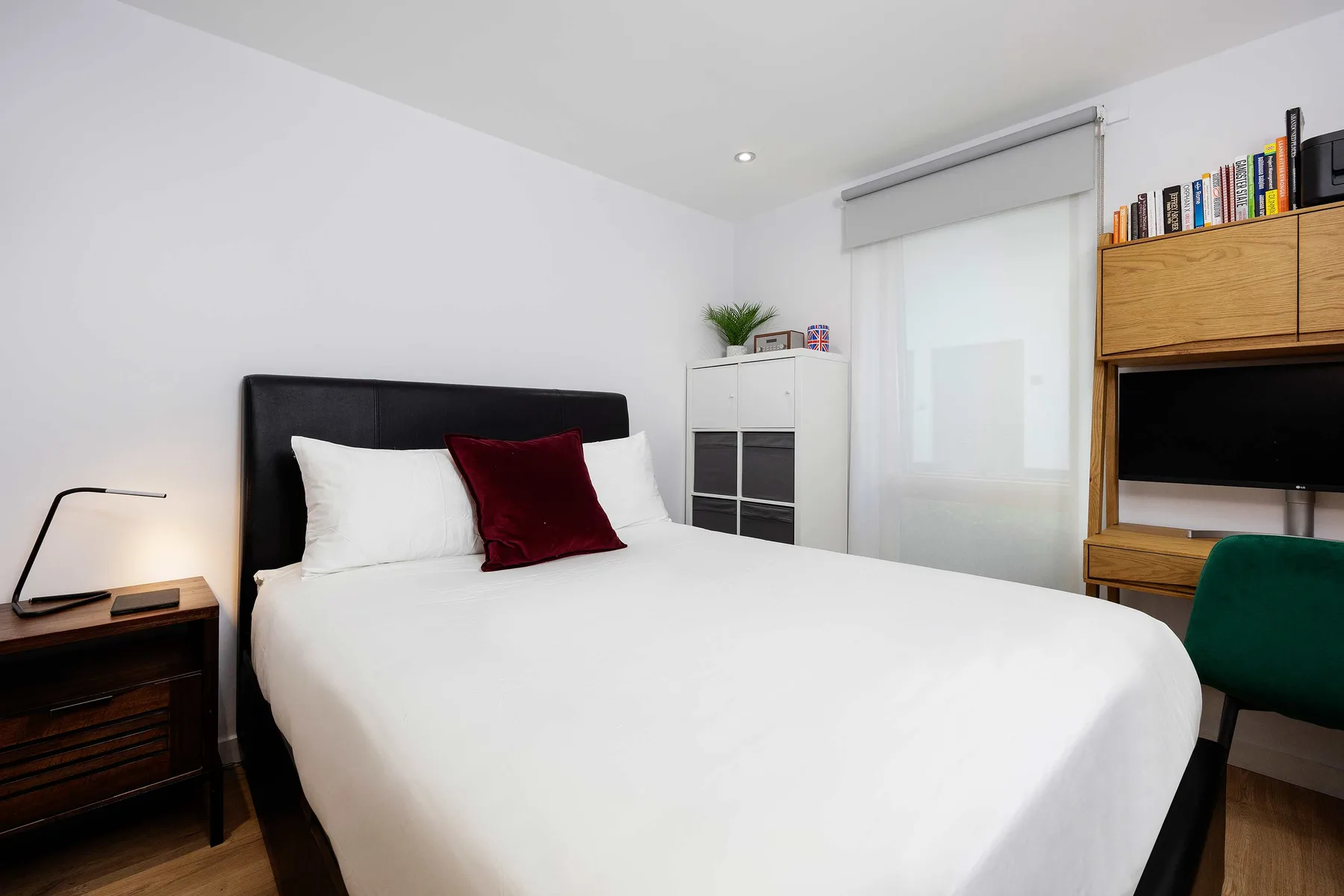 A bright bedroom with a neatly made bed and a wooden desk area.