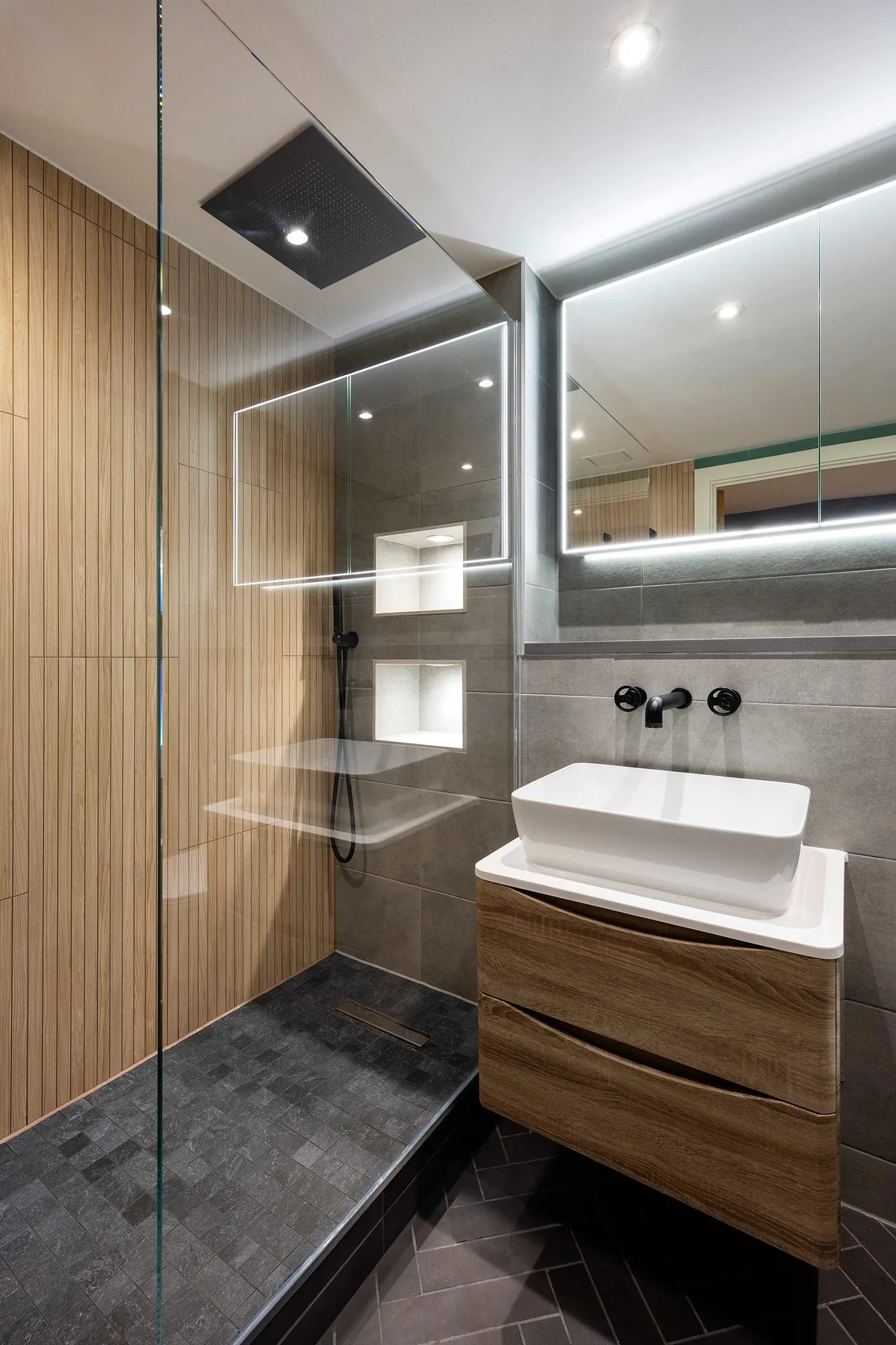 A modern bathroom features a glass shower beside a vessel sink and mirror.