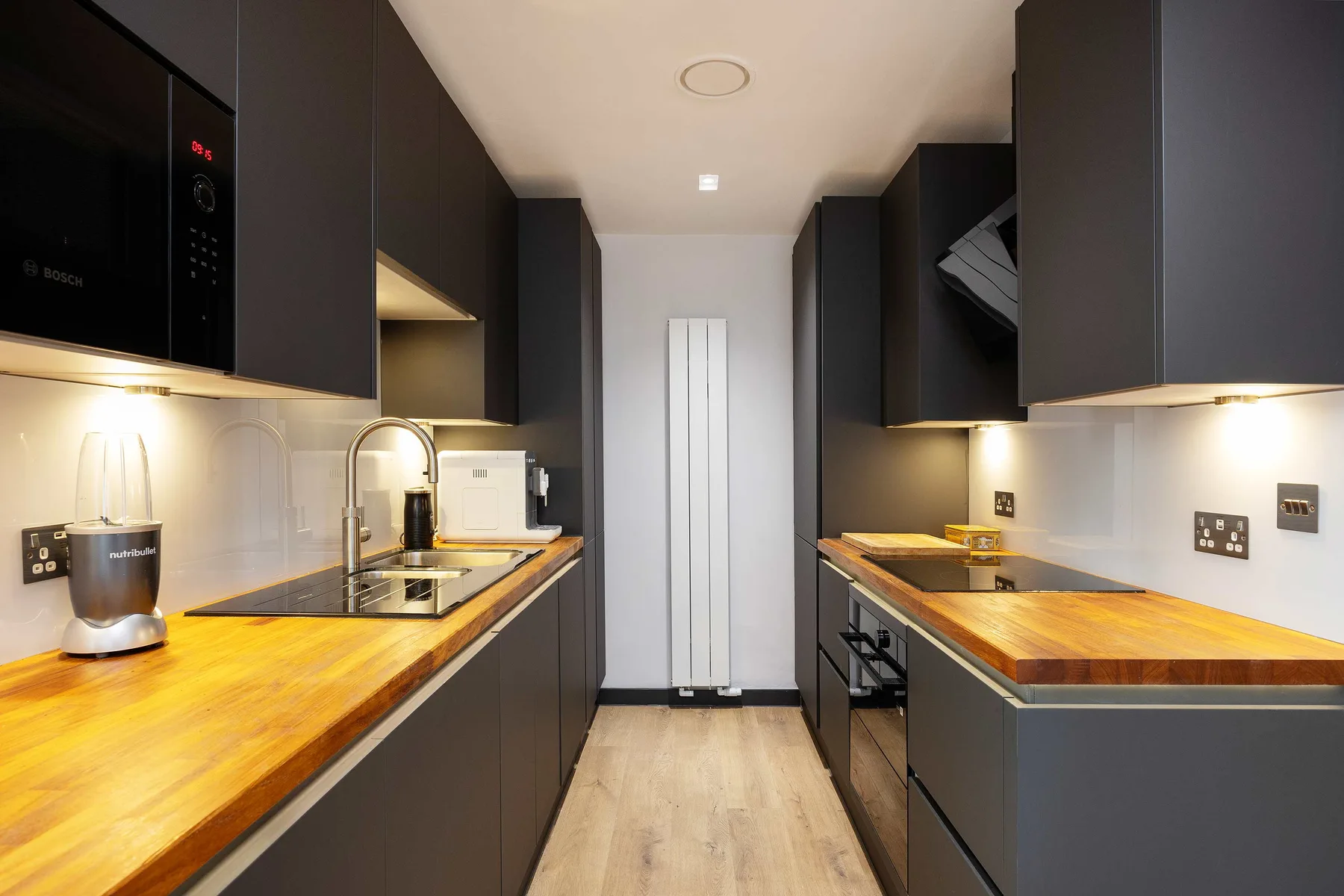 A narrow modern kitchen with wood countertops and dark cabinets.