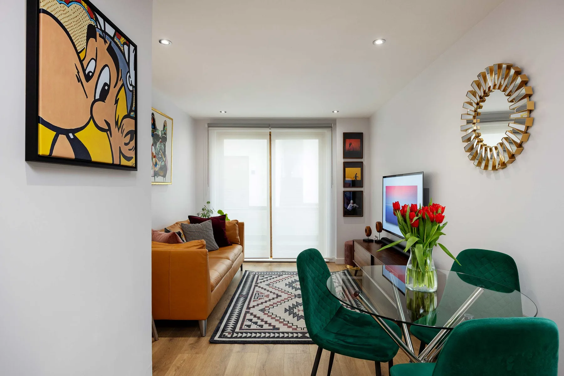 A bright living room with seating, a glass dining table, and colorful wall art.