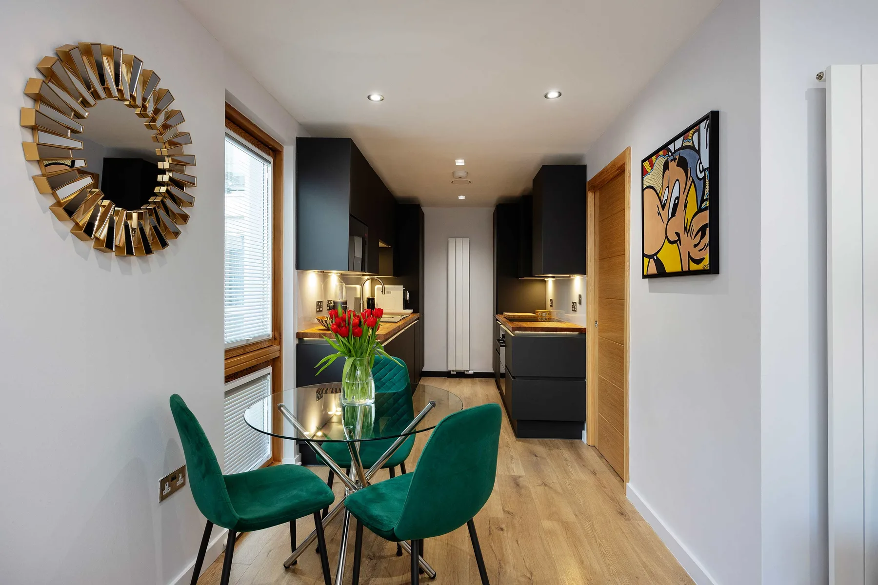 A narrow kitchen and dining area with green seating and a glass table.