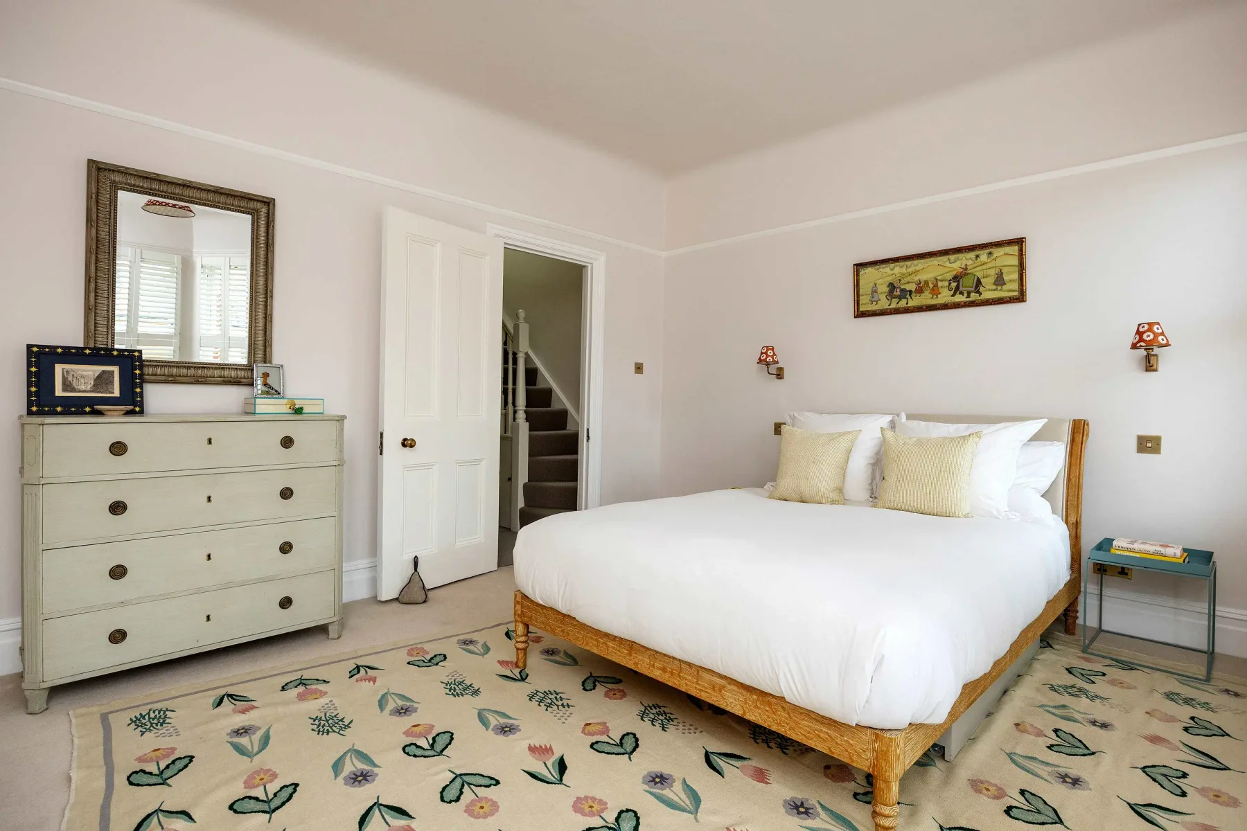Un dormitorio luminoso con una cama blanca y una alfombra estampada.
