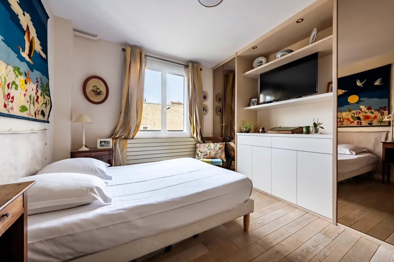 A bedroom with a bed, window, and built-in shelving with a television.