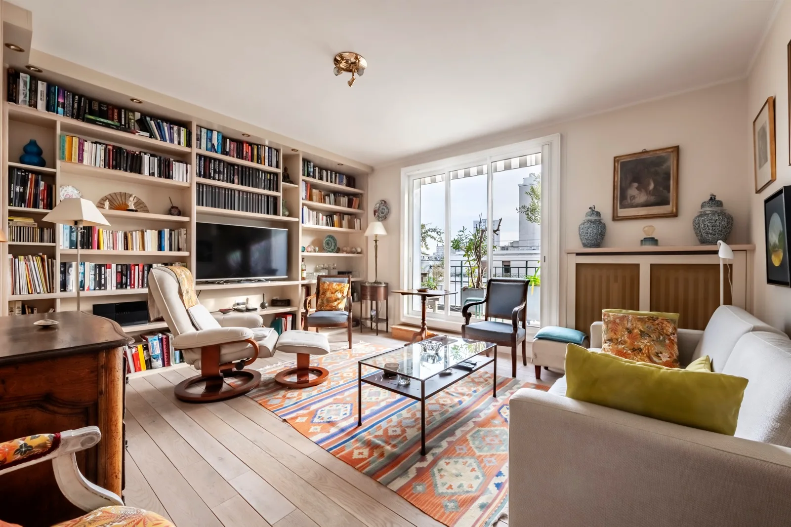 Una sala luminosa con estanterías, asientos y puertas de vidrio que dan a un balcón.