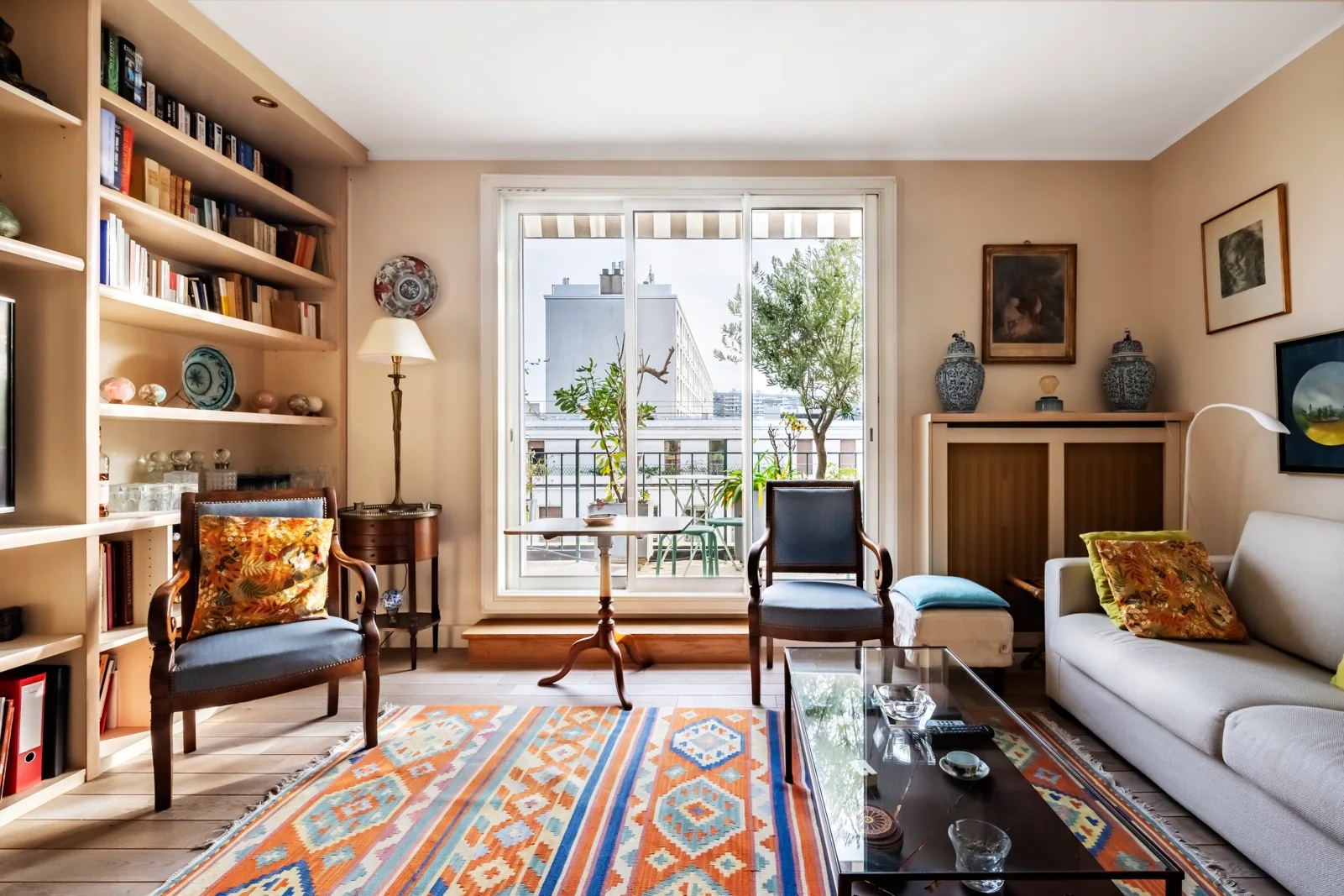 A bright living room with bookshelves, seating, and large windows overlooking greenery.