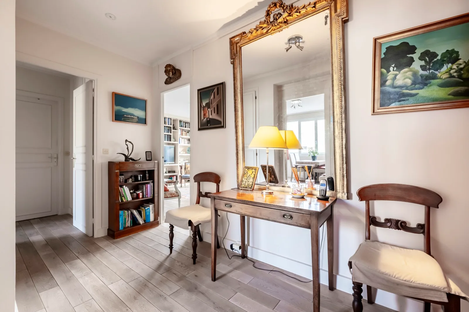A bright room with a wooden writing desk, chairs, and a large wall mirror.