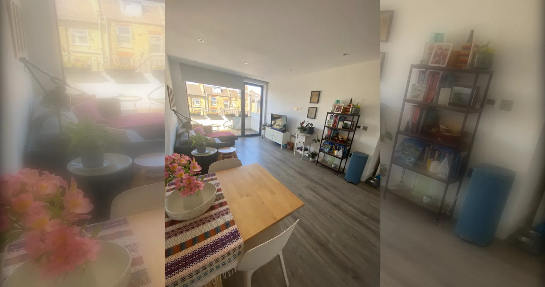 A bright living area with a wooden table and shelving beside large windows.