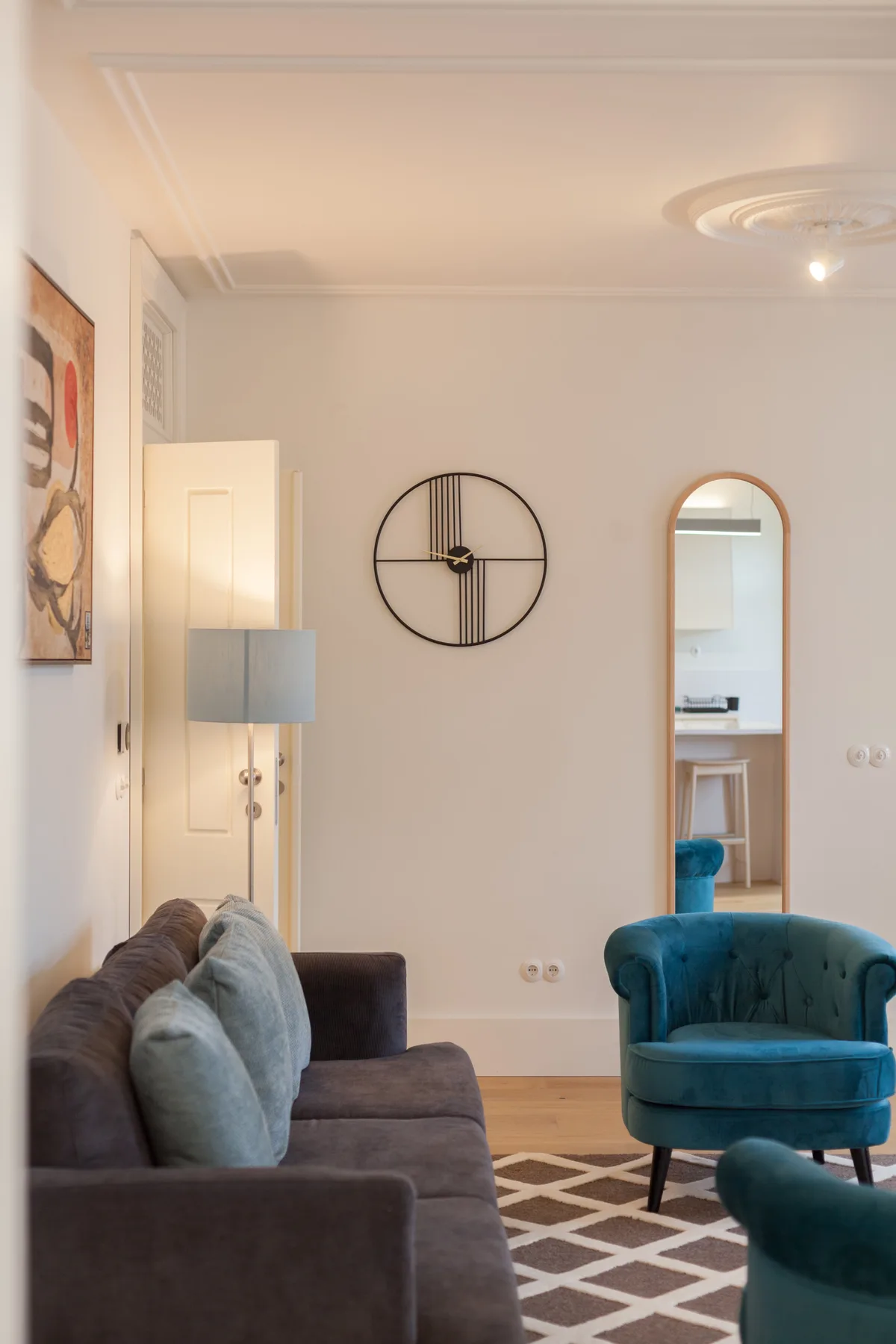 Una sala de estar con un sofá, asientos color turquesa y un reloj redondo.