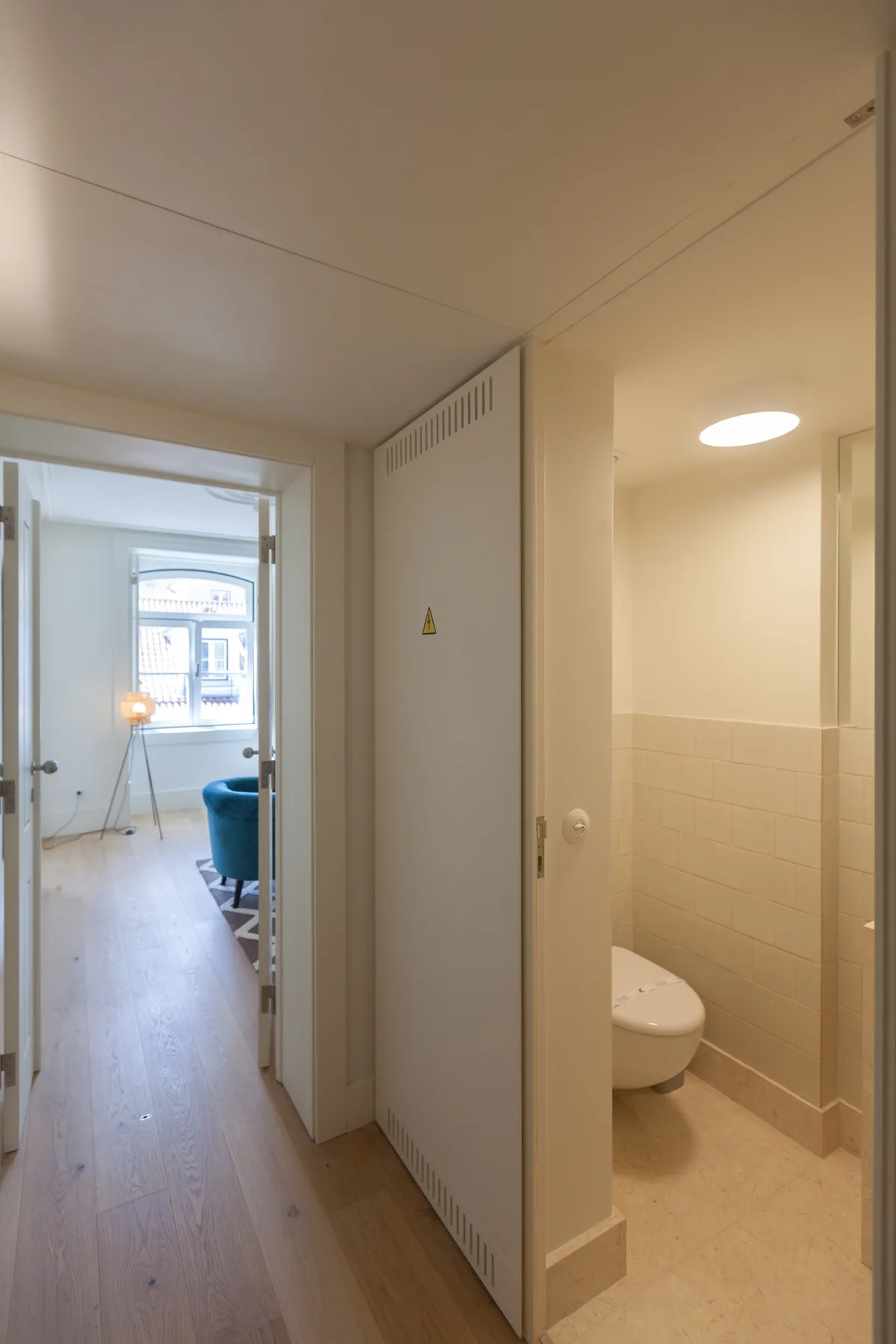 Un pasillo conduce a un baño con inodoro y a una habitación luminosa al fondo.