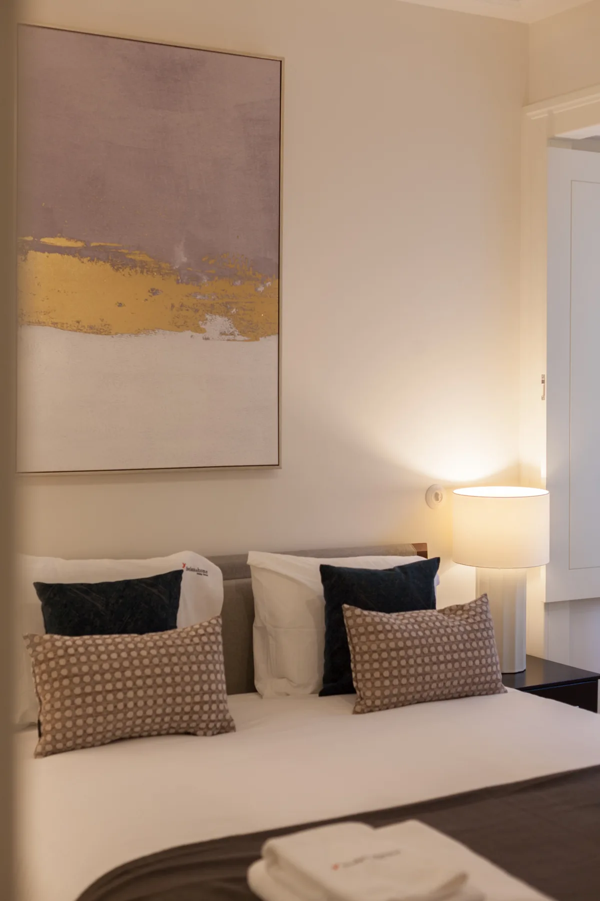 Un dormitorio con una cama tendida, cojines estampados y arte abstracto en la pared.