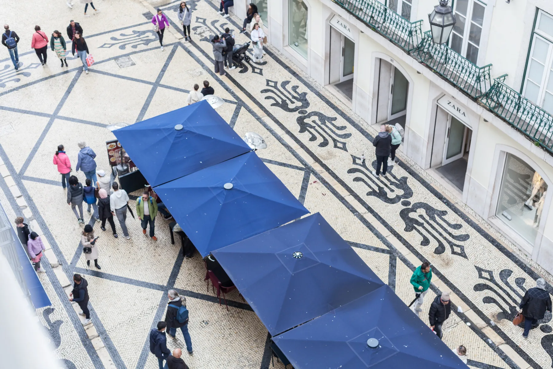 Una calle peatonal comercial con pavimento decorado y toldos azules.