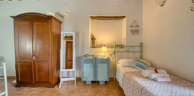 A bedroom with a single bed, a wooden wardrobe, and a small cabinet.