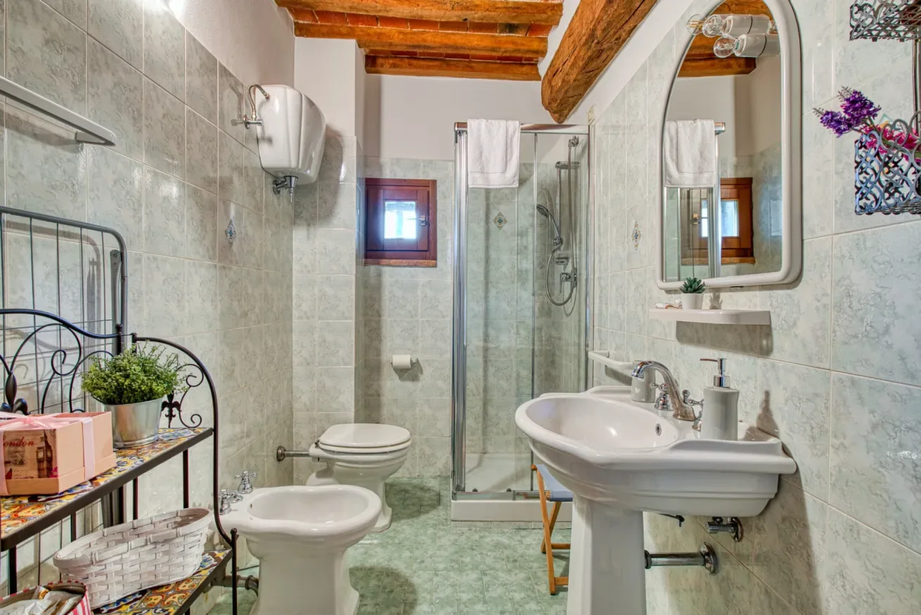 A tiled bathroom with a shower, toilet, and sink beneath exposed wooden beams.