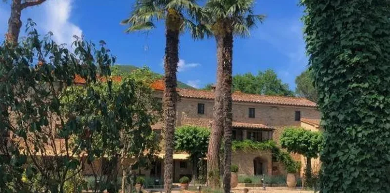 A two-story building stands among trees and palms under a clear blue sky.
