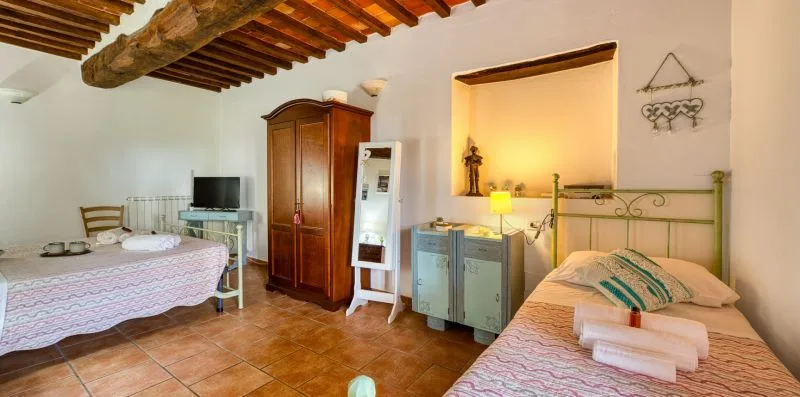 A bedroom with two beds, a wardrobe, and a television beneath exposed ceiling beams.