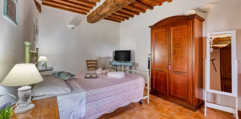 A bedroom with a bed, wooden wardrobe, and exposed ceiling beams.