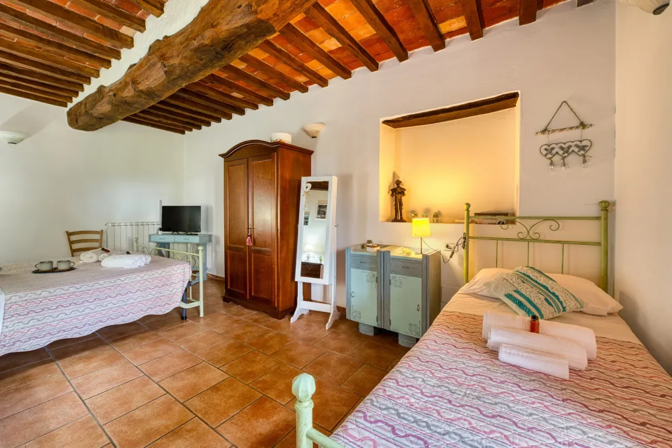 A bedroom with two beds, a television, and exposed wooden ceiling beams.