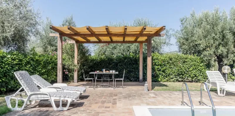 A paved patio with lounge seating, a table, and a wooden pergola.