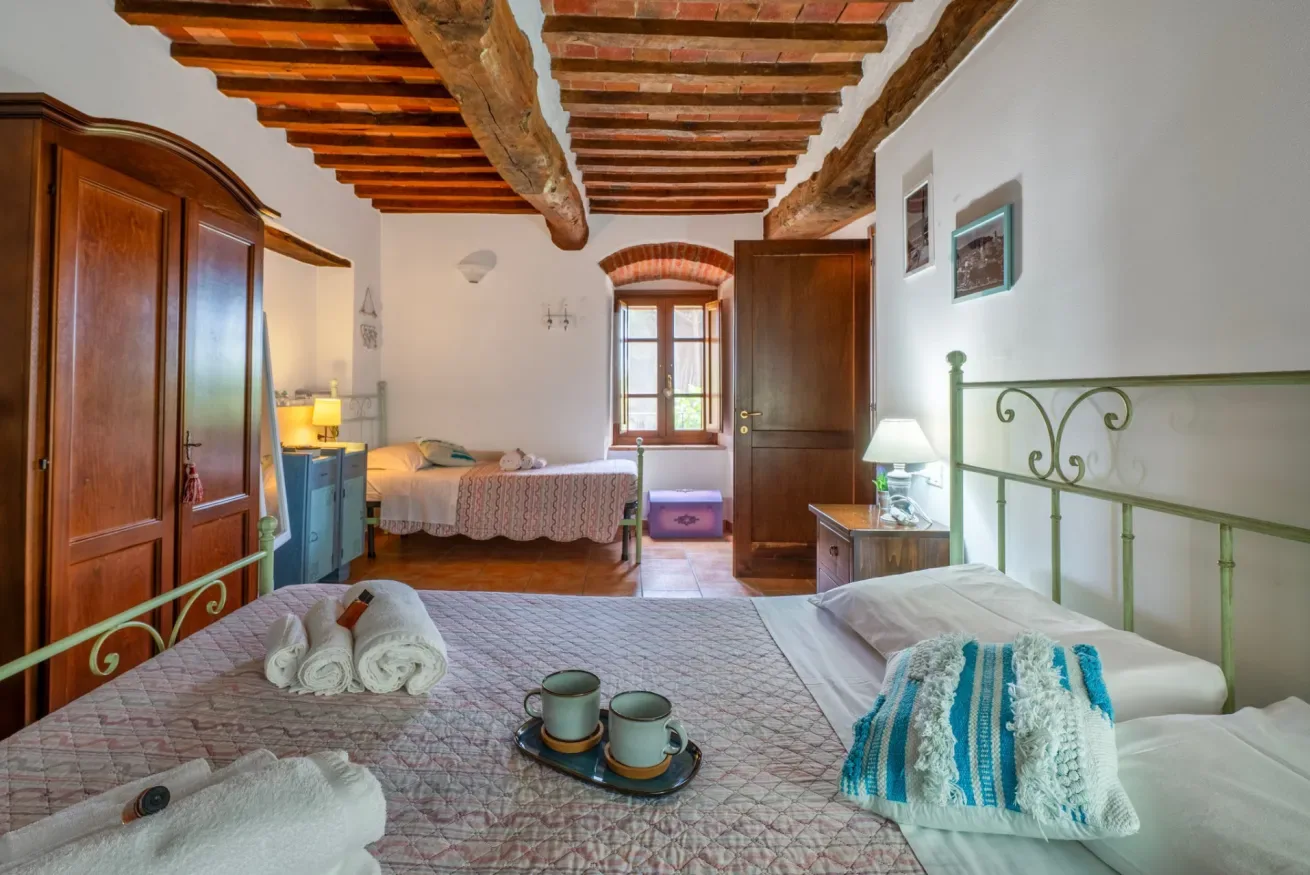 A bedroom with a bed, wooden ceiling beams, and a window.