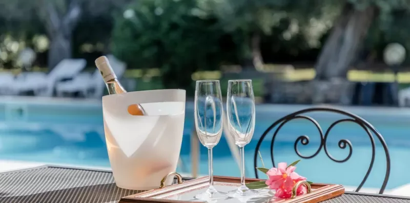 A poolside table holds a drink bucket, two glasses, and a small flower arrangement.