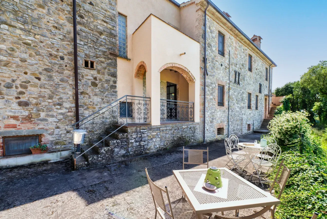 A stone building opens onto a paved outdoor patio with tables and chairs.