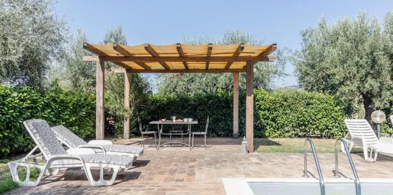 An outdoor patio with a wooden pergola, seating, and a pool edge.