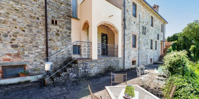 A stone building with an arched entrance and outdoor seating on a patio.