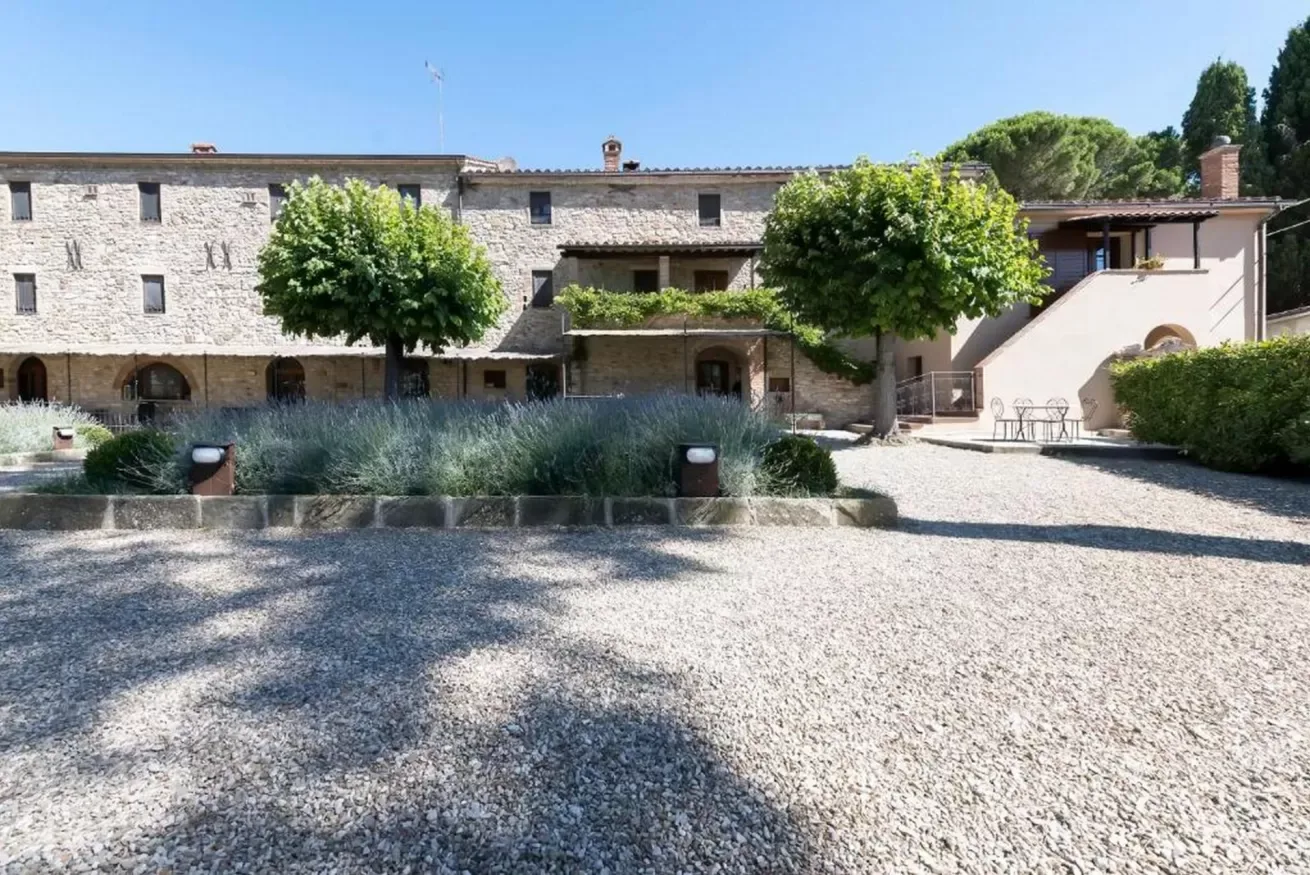 A stone building faces a gravel courtyard with trees and planted beds.