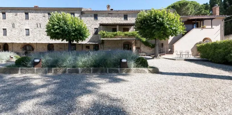 A stone building overlooks a gravel courtyard with trees and planted beds.