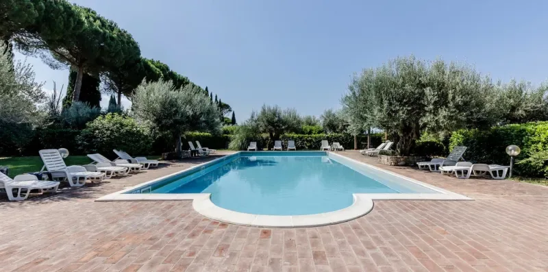 An outdoor swimming pool is surrounded by paved patio space and lounge seating.