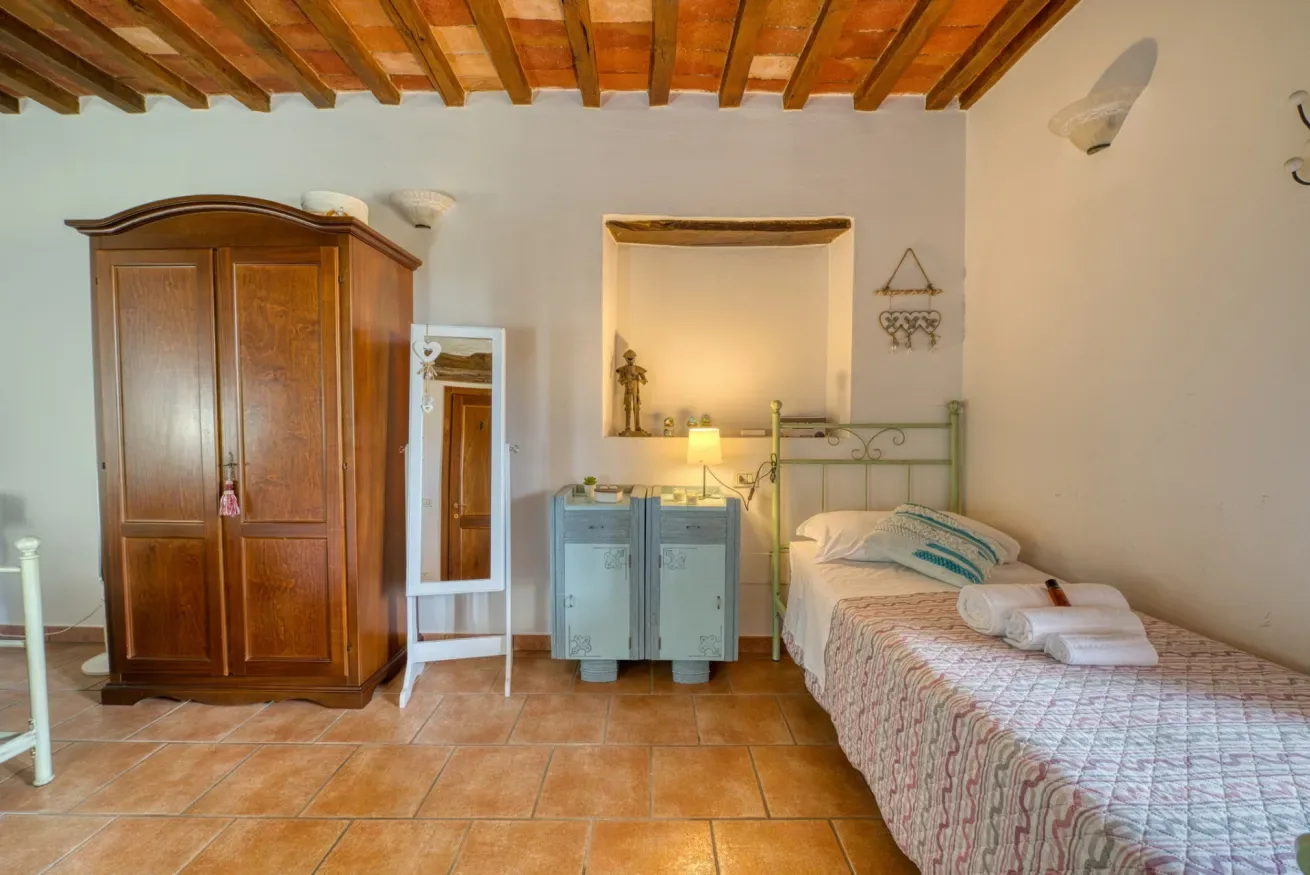 A bedroom with a metal bed, wooden wardrobe, and exposed ceiling beams.