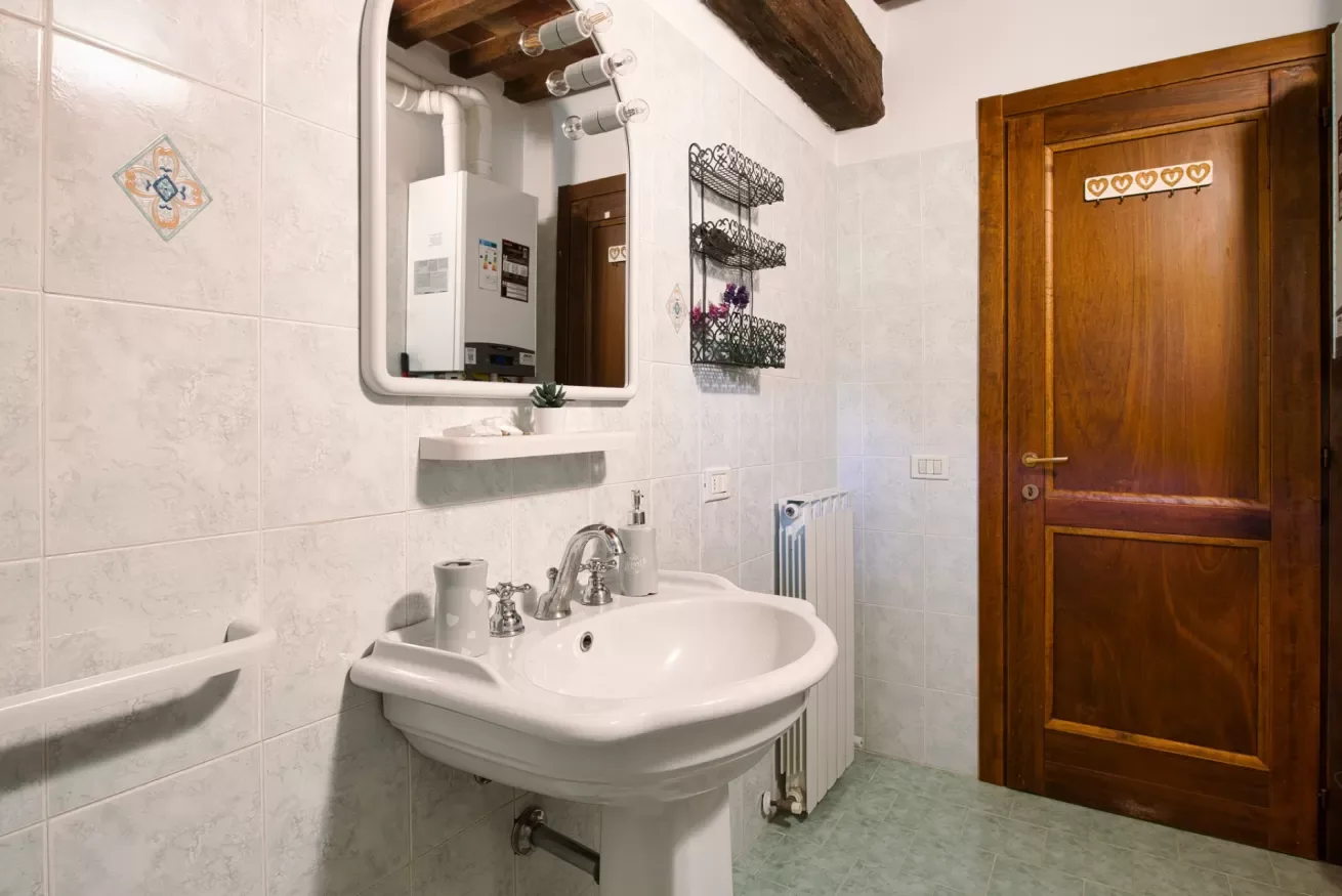 A tiled bathroom with a sink, mirror, and wooden door.