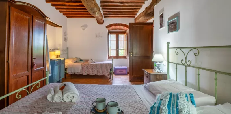 A bedroom with two beds, wooden ceiling beams, and a window.