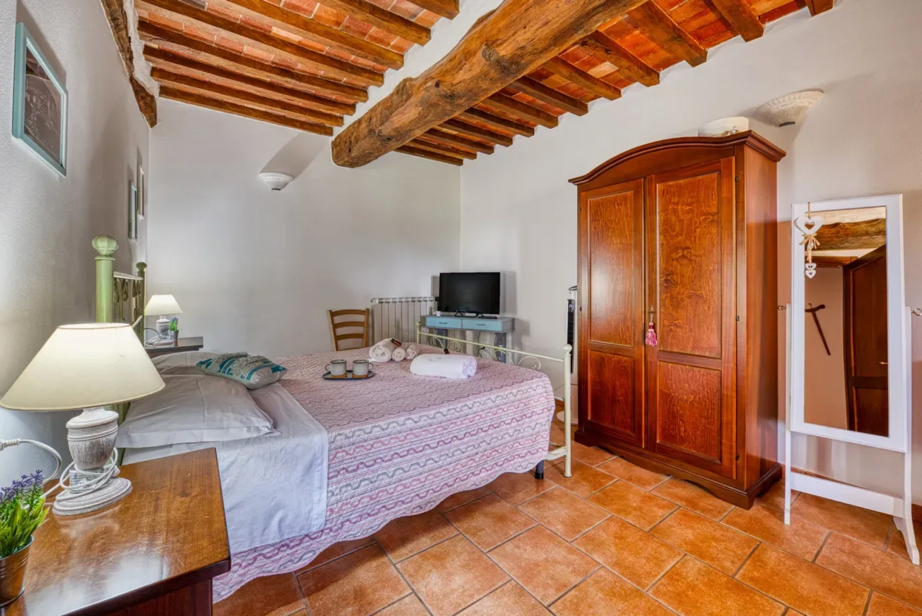 A bedroom with a bed, wooden wardrobe, and exposed ceiling beams.