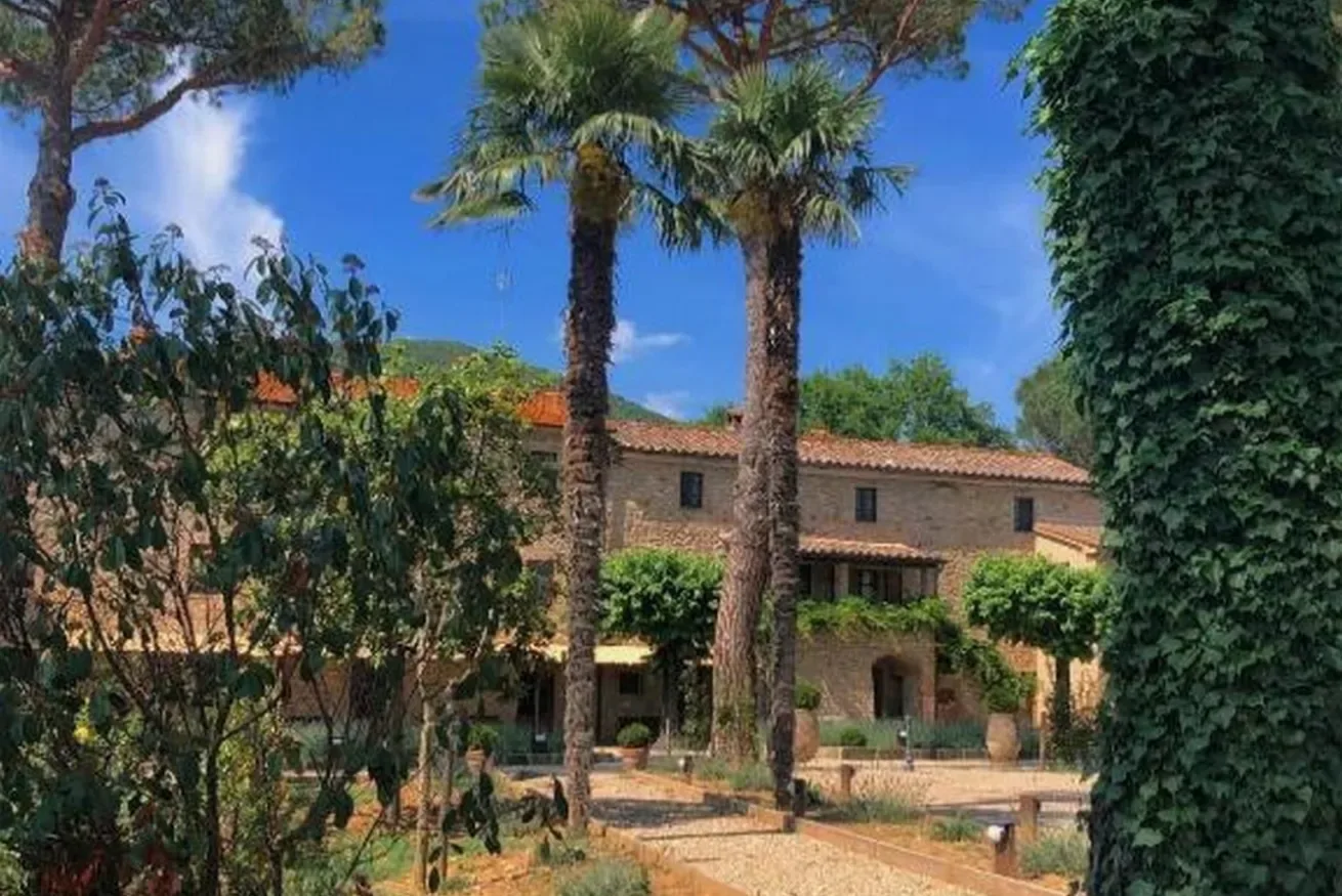 A stone building stands behind a garden with palm trees.