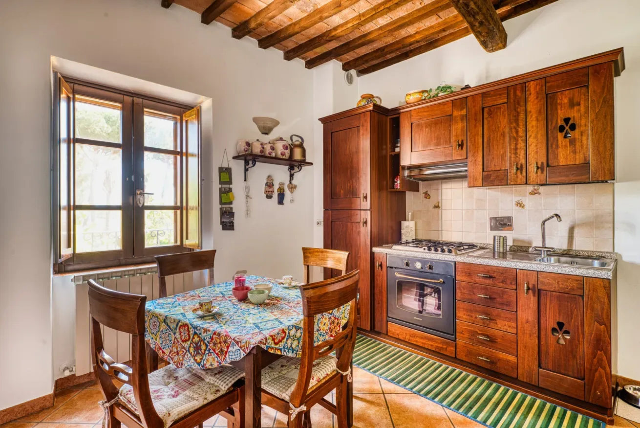 A kitchen dining area with wooden cabinets and a table covered in a colorful cloth.