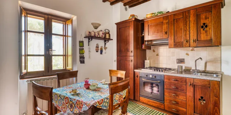 A rustic kitchen with wooden cabinets, a stove, and a dining table by the window.