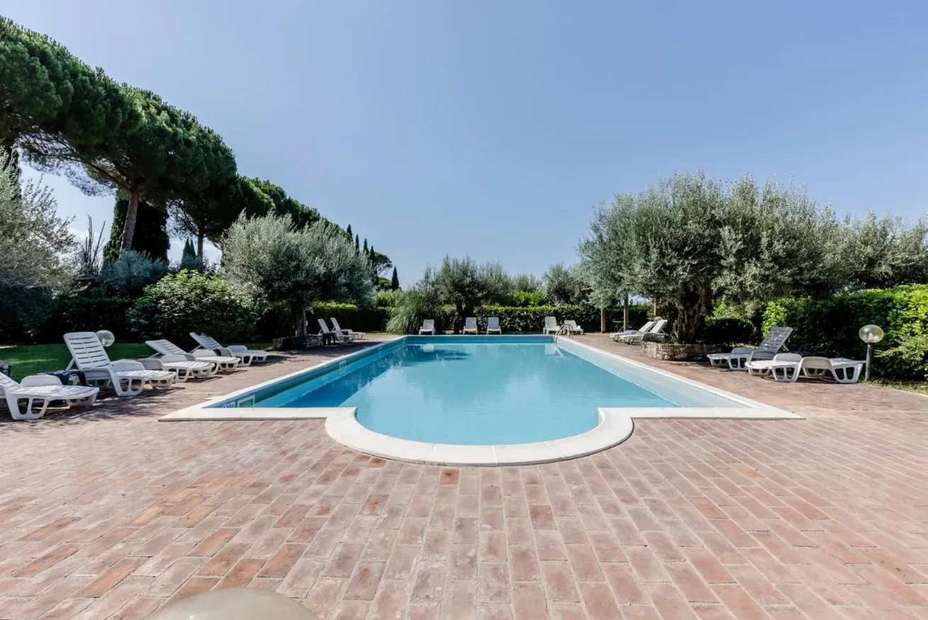 An outdoor swimming pool is surrounded by a brick-paved deck and lounge chairs.