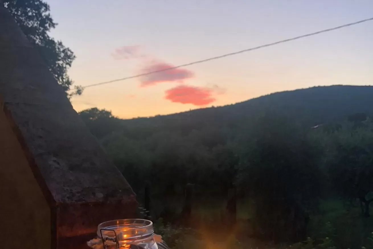 A sunset glows above a wooded hillside, with a drink on an outdoor ledge.