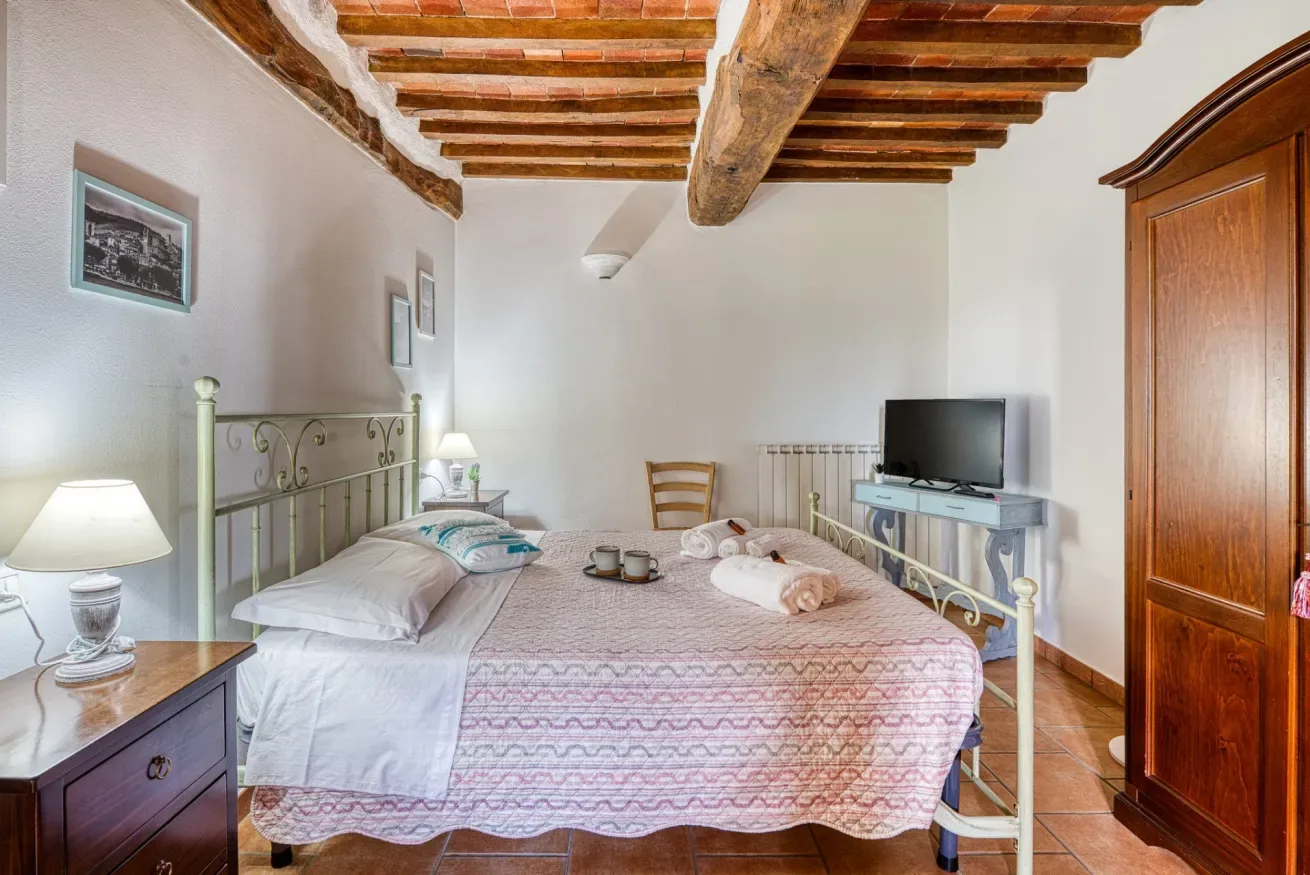 A bedroom with a bed, a television, and exposed wooden ceiling beams.