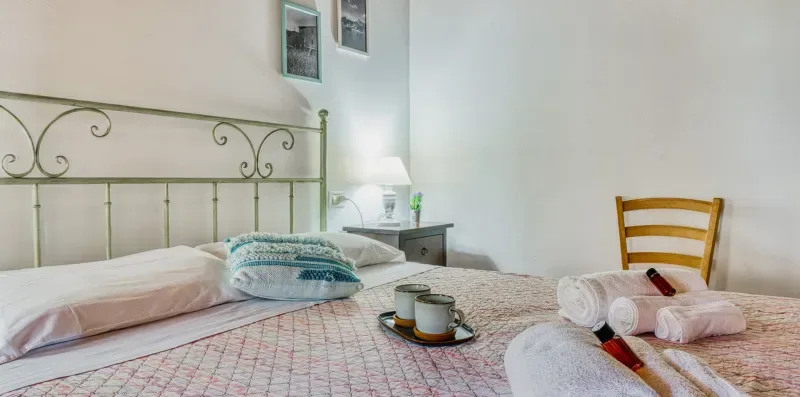 A bedroom with a neatly made bed, folded towels, and a wooden chair.