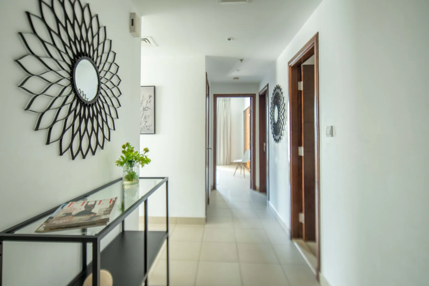 Un pasillo luminoso con una consola de tapa de vidrio y espejos decorativos en la pared.