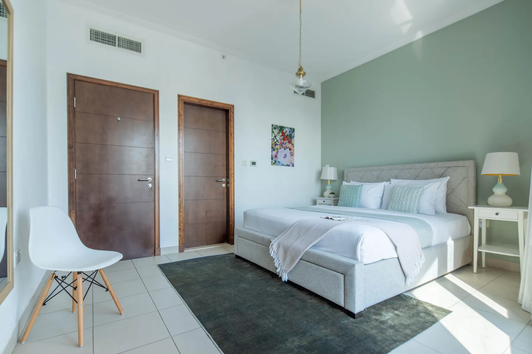 Dormitorio con una cama frente a una pared verde y dos puertas de madera.
